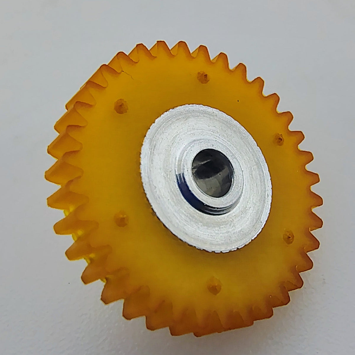 A small circular orange plastic gear or roller with a white center hub and a dark screw hole, photographed on a plain light gray surface.